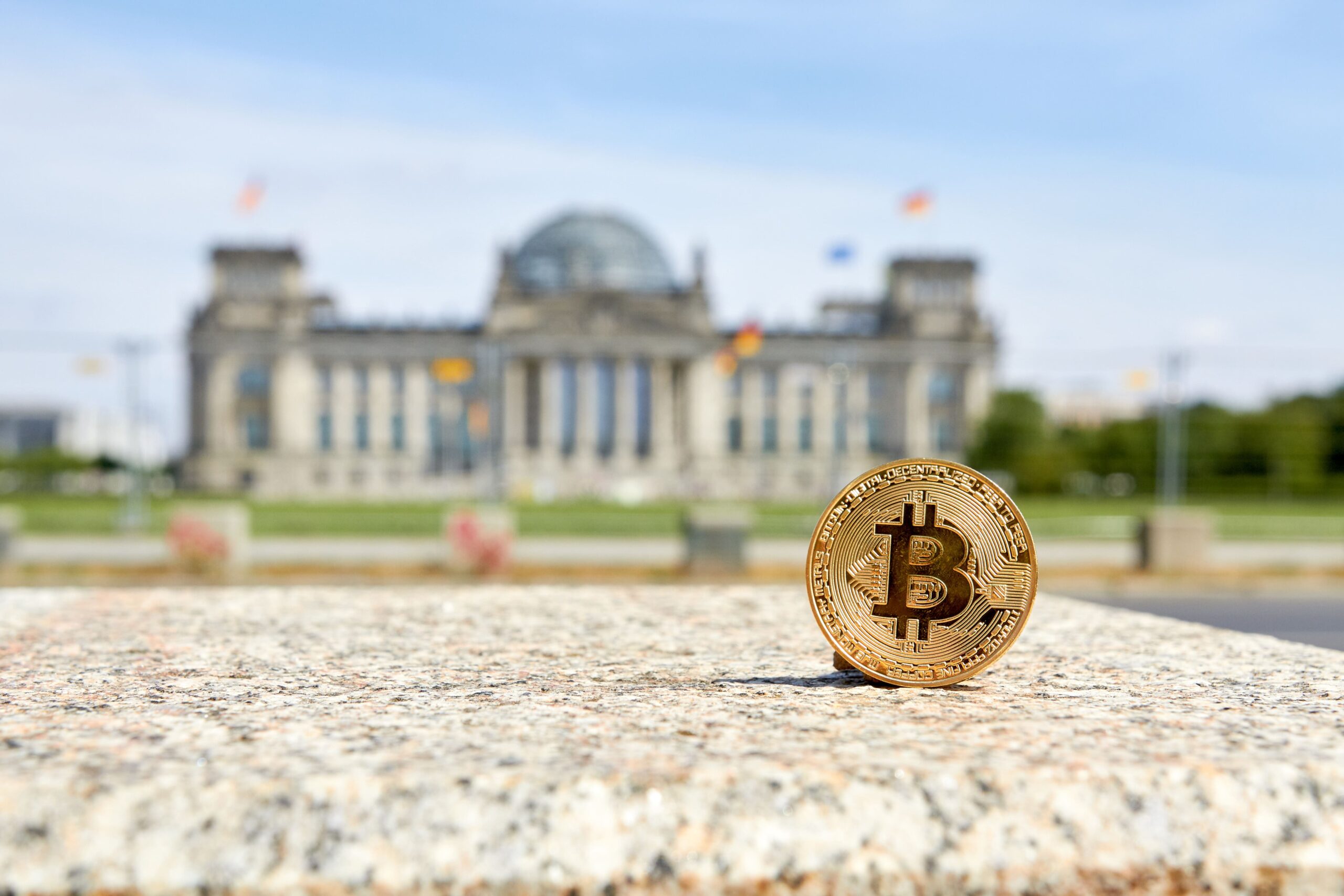 Bitcoin-Münze im Fokus vor dem unscharfen Hintergrund des Reichstagsgebäudes in Berlin, Symbol für Kryptowährung in der Politik